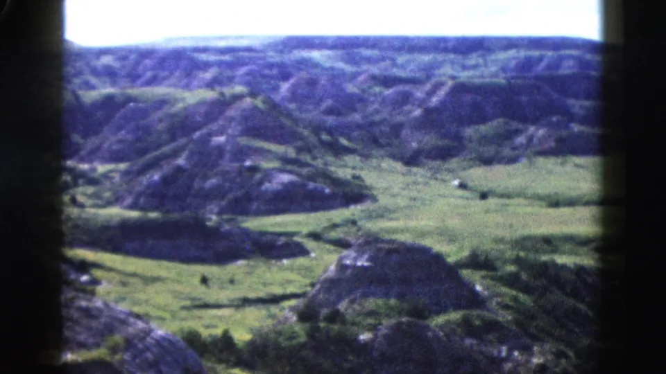 8mm archival frame c.1958 from a high overlook showing rolling green hills and eroded ridgelines in Wyoming wilderness.