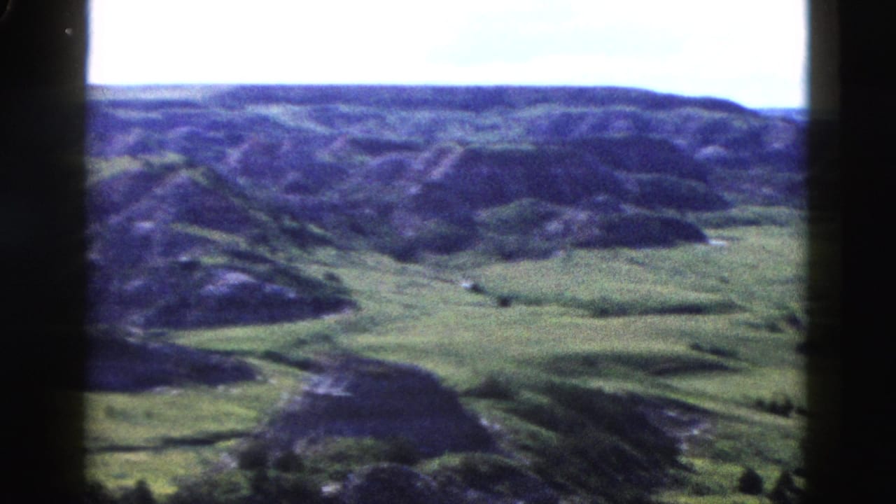 8mm color shot of eroded ridgelines and green valley floor filmed from an elevated viewpoint with dark frame vignetting.