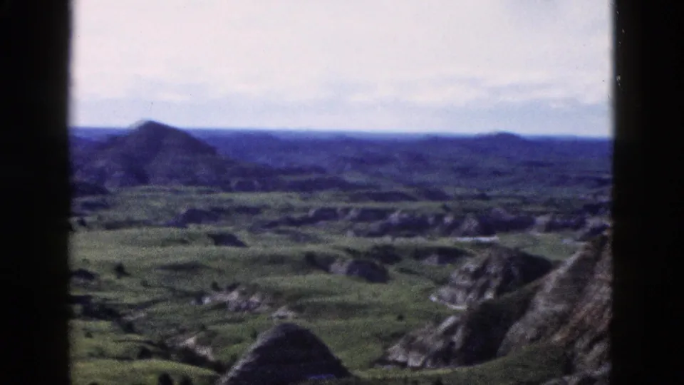 8mm home-movie pan endpoint: conical buttes and eroded terrain across a wide Wyoming valley, Yellowstone area, circa 1958.