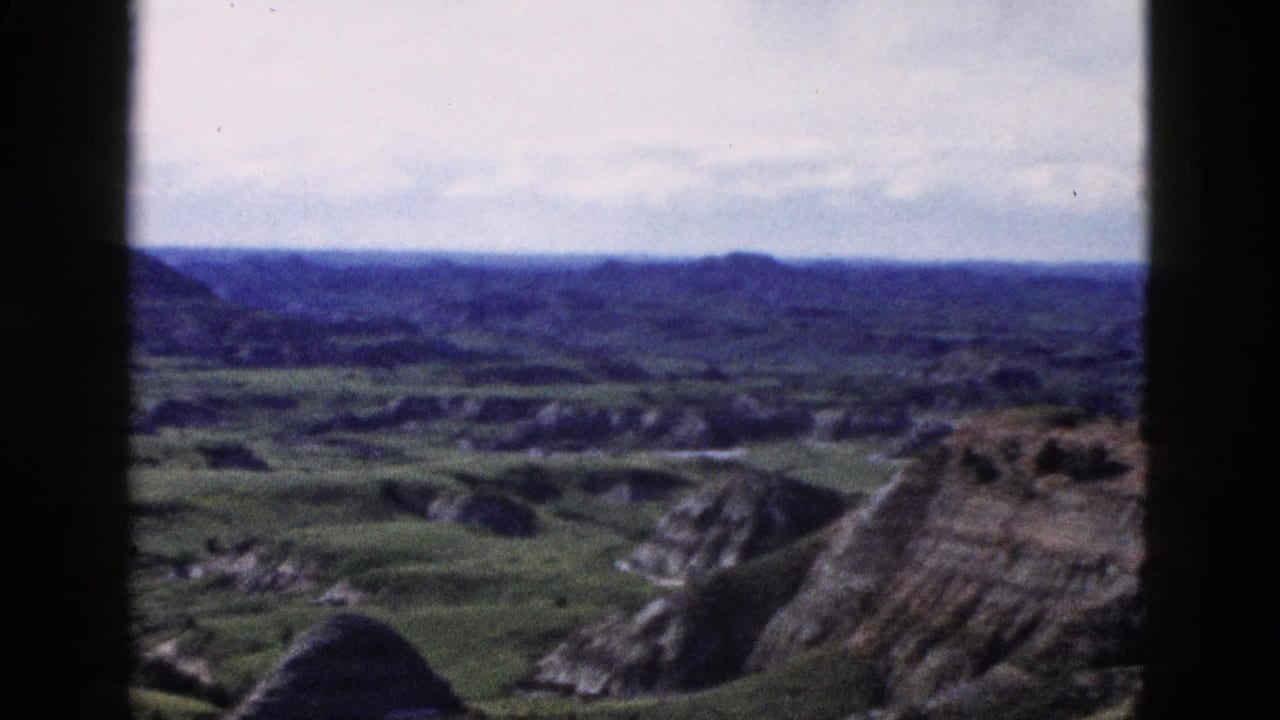 Elevated 8mm color view of layered badlands-type rock formations and green valley, attributed to Wyoming area, circa 1958.