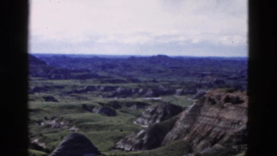 Elevated 8mm color view of layered badlands-type rock formations and green valley, attributed to Wyoming area, circa 1958.