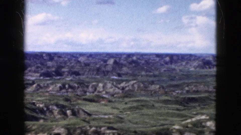 Wide 8mm panoramic view of eroded badlands-type terrain under cumulus clouds, Wyoming area, circa 1958.