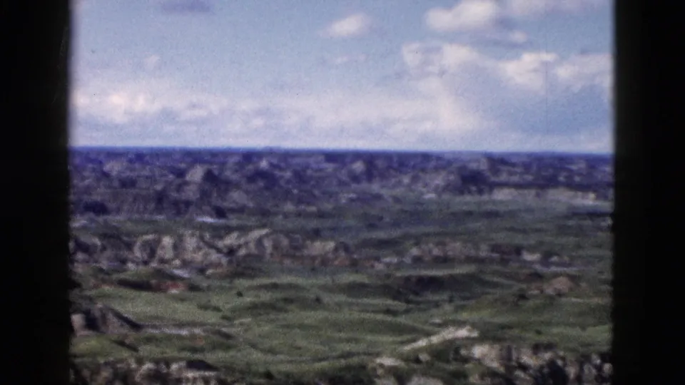 Wide 8mm pan across rugged eroded terrain under partly cloudy sky, Wyoming area, circa 1958.