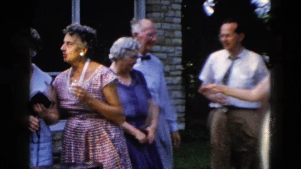 Small group in late-1950s attire socializing at an outdoor gathering; woman in plaid dress holds a drink, circa 1958.