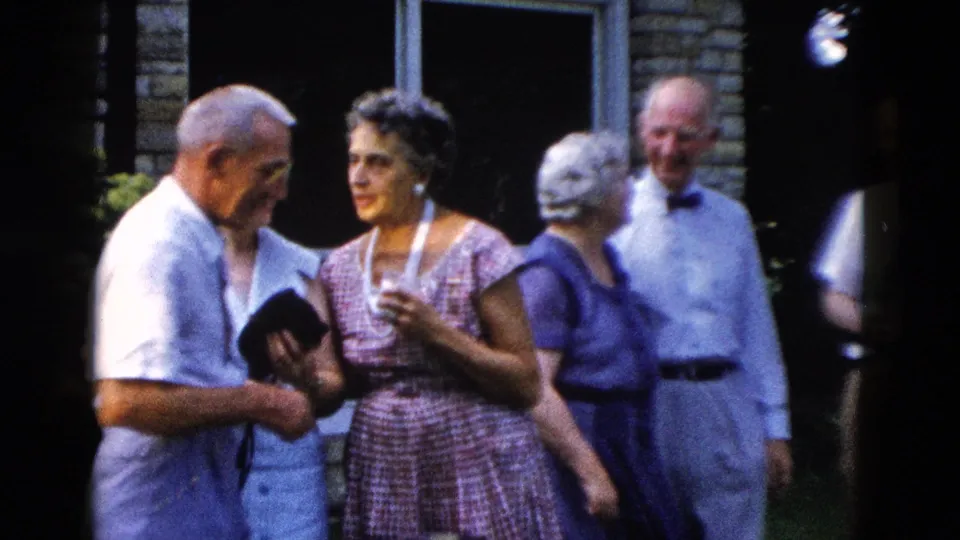 Close view of four adults at a 1950s outdoor social event; older man and woman in plaid dress in foreground with two guests behind, circa 1958.