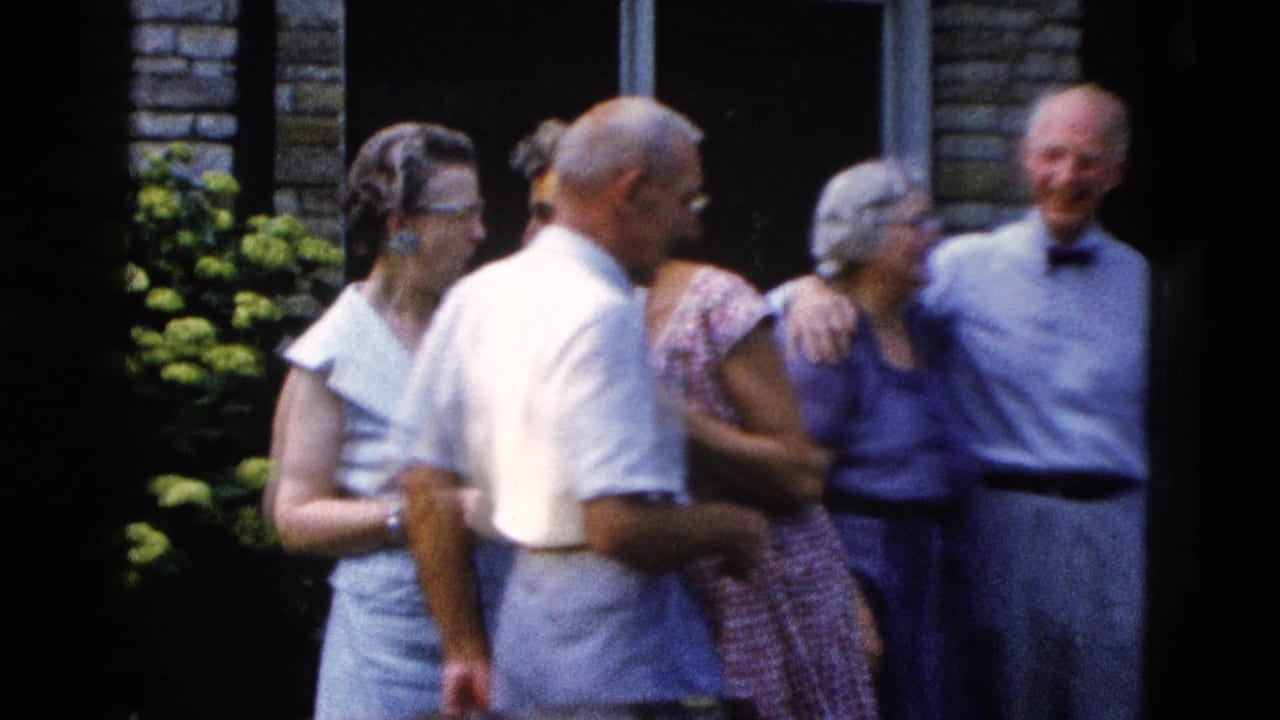Five adults in late-1950s dress attire gathered outdoors before a masonry wall, smiling and conversing; 8mm home movie, Wyoming, circa 1958.