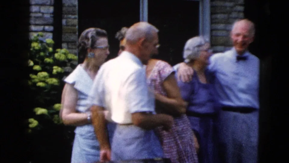 Five adults in late-1950s dress attire gathered outdoors before a masonry wall, smiling and conversing; 8mm home movie, Wyoming, circa 1958.