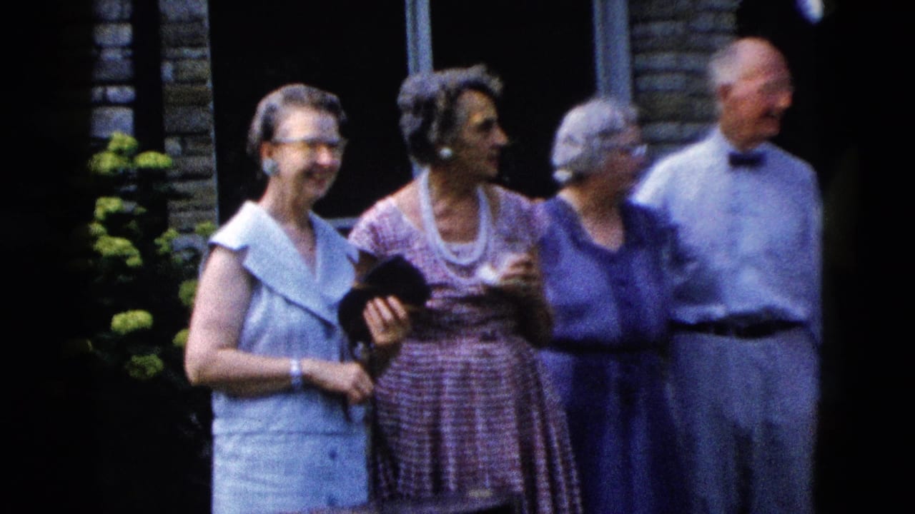 Closer view of four adults outside a brick-faced building; women in dresses, man in bow tie, green foliage behind.