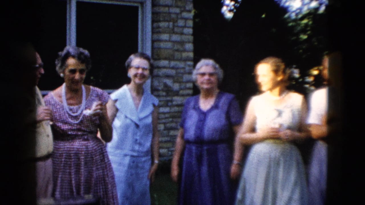 Five or six people, mostly older women in mid-century blue and purple dresses with pearl necklaces, gathered outdoors near a light brick building, circa 1958.