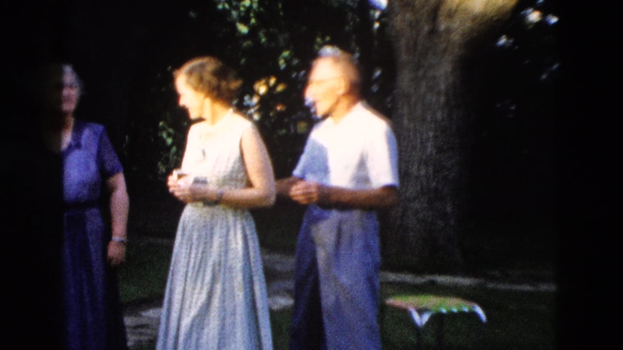 c. 1958 outdoor gathering in Wyoming: young woman in light sleeveless dress and man in white shirt in conversation; elderly woman in purple dress stands behind them beneath a shade tree.