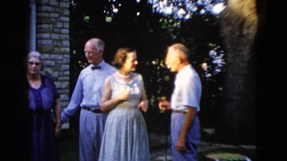 c. 1958 family gathering in Wyoming: elderly man with bow tie, young woman in light dress with pearl necklace, and man in white shirt grouped near a brick structure; elderly woman partially visible at far left.