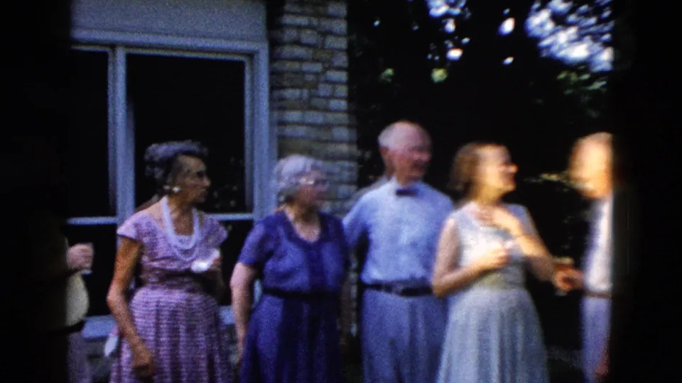 Five older adults socializing in a backyard, reportedly Wyoming circa 1958; brick house facade, large windows, and blooming hydrangeas in background.