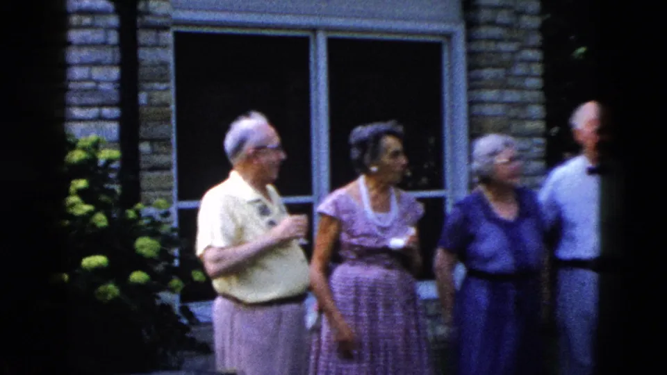 Four older adults at a backyard gathering, reportedly Wyoming circa 1958; hydrangea bushes in full bloom, brick house with large windows behind them.