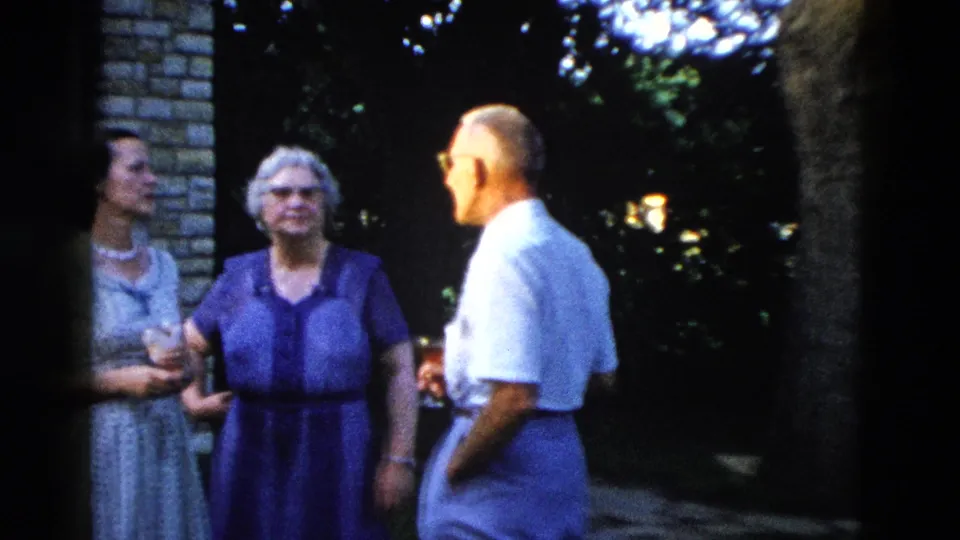 Continuation of an outdoor family gathering, circa 1958 Wyoming; two women and a man interact informally against an evening backdrop of foliage and ambient light.
