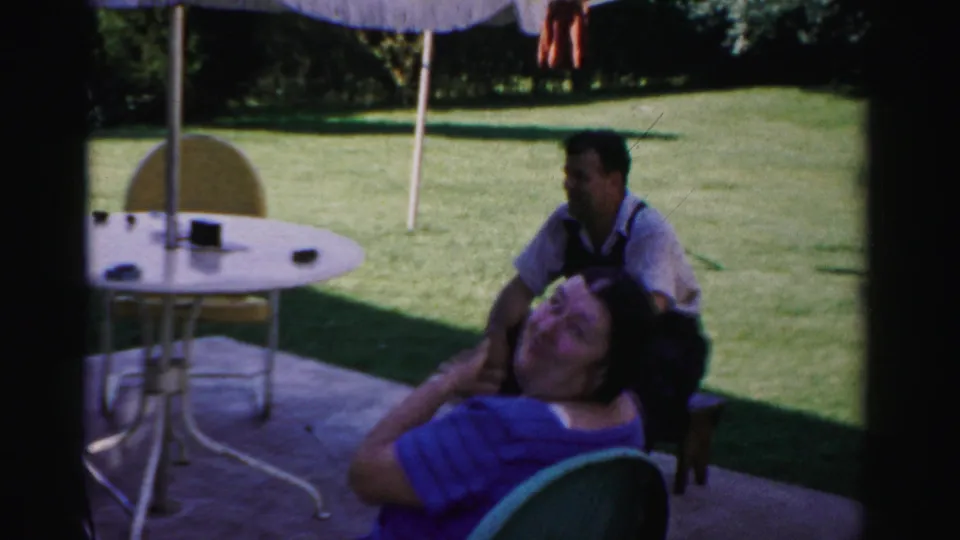 In Catskill, New York in 1957, adults sit and talk on a shaded patio beside a round table and umbrella with lawn in the background.