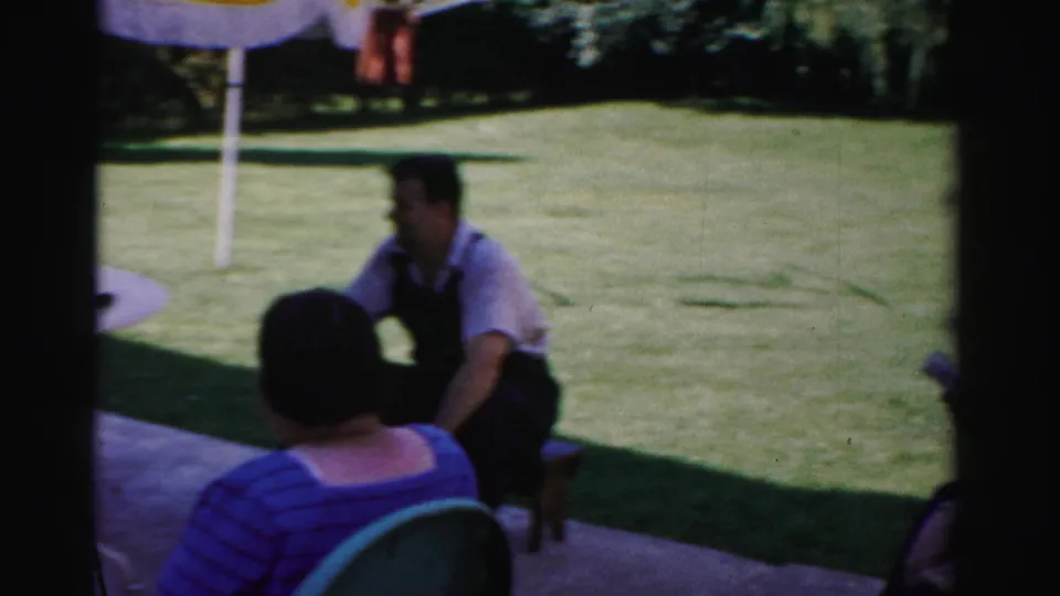 A woman in a blue striped top faces a seated man on a small stool during a 1957 Catskill outdoor gathering.