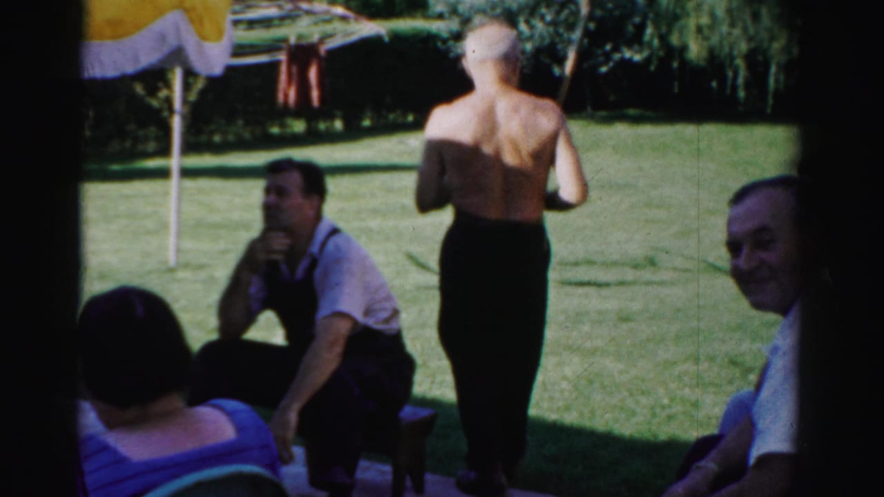 Adults sit and stand on a sunny backyard lawn near a shaded bench and clothesline.