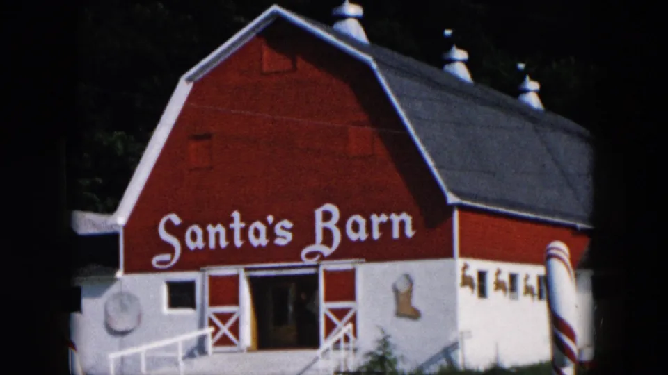1957 Hicksville, New York frame of the Santa's Barn exterior, with the painted sign, ramp, open doorway, and holiday props visible.