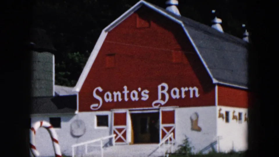 1957 Hicksville, New York 8mm frame with a closer view of the Santa's Barn sign, red facade, white trim, ramp, and adjacent structure.