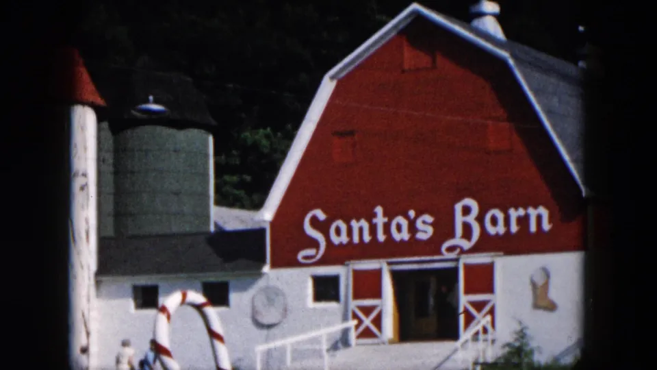 1957 Hicksville, New York frame showing the Santa's Barn exterior with holiday decorations, a ramp, and small visible visitors near the building.
