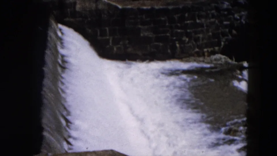 Closer 8mm frame of water flowing over the dam structure in the Hicksville river scene.