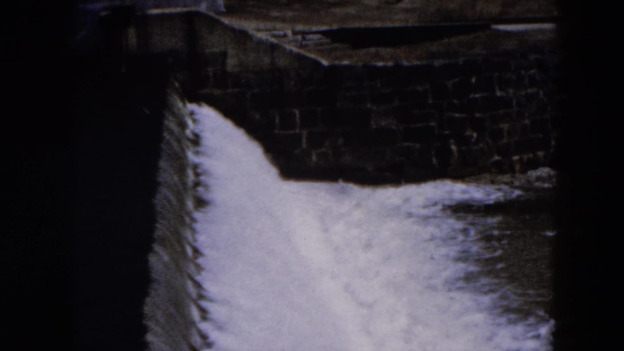 White water flows beside a dark stone wall in a narrow spillway channel.