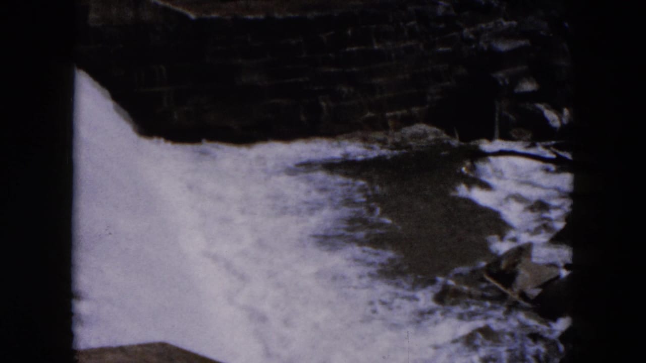 Water spreads across a dark channel with rocks and stonework near the right edge.