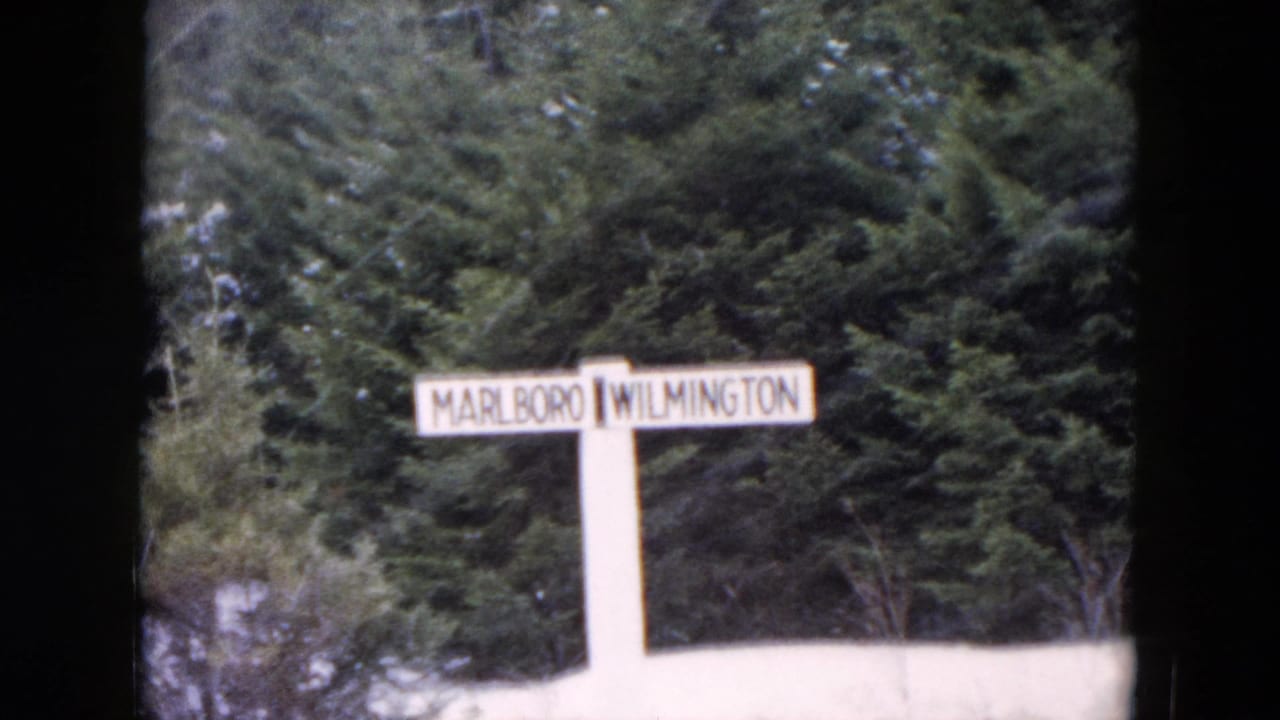 White directional sign reading Marlboro and Wilmington beside snow and evergreen trees.