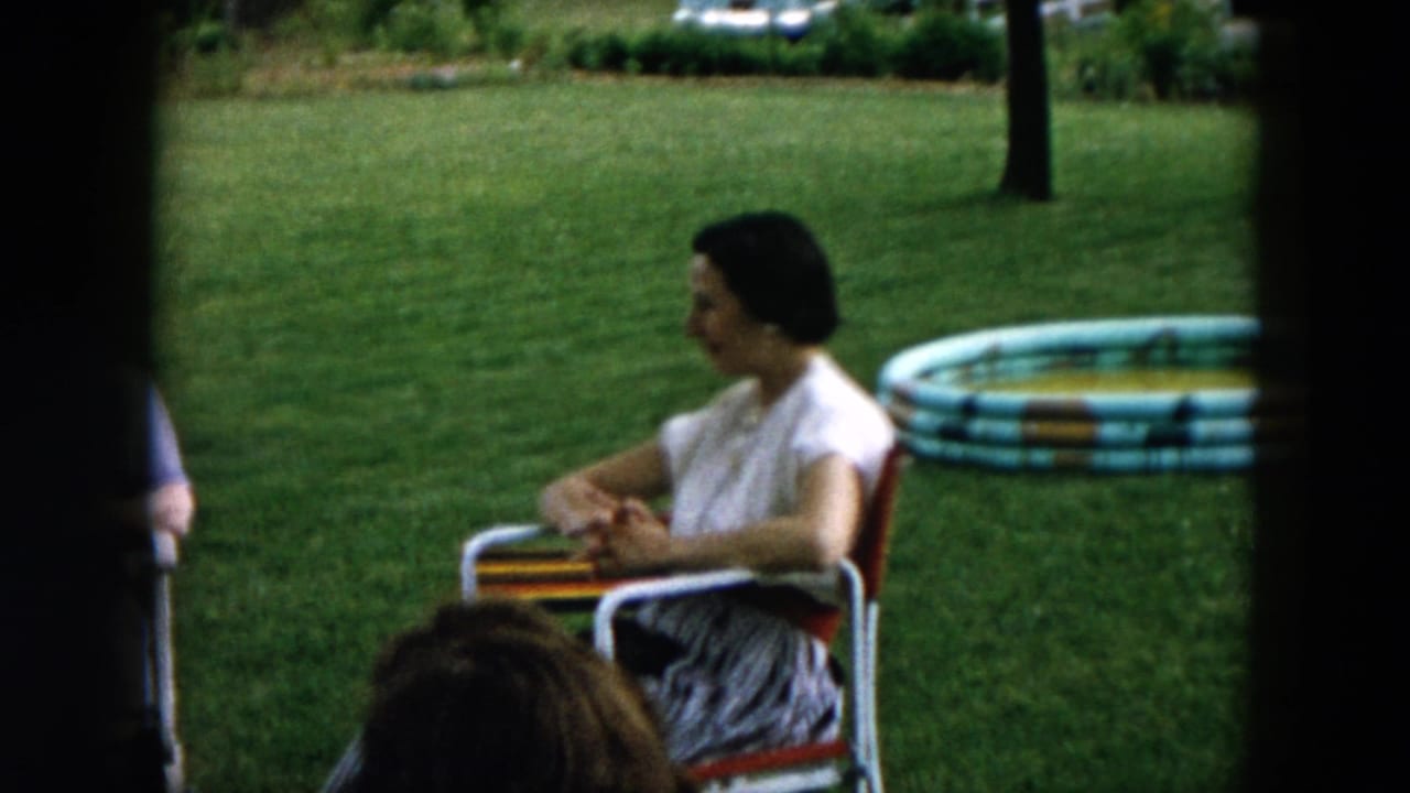 Woman seated in a lawn chair beside a striped inflatable pool on a grassy yard.
