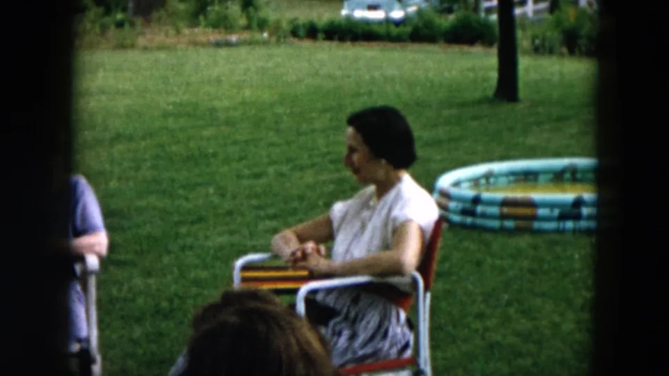 A 1957 Hicksville backyard view shows a woman seated in profile near a striped inflatable pool, with grass and trees in the background.