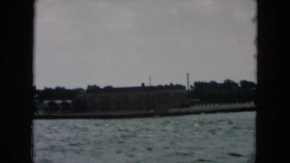 Industrial waterfront buildings appear across the harbor, filmed from a moving boat with soft focus and dark frame edges.