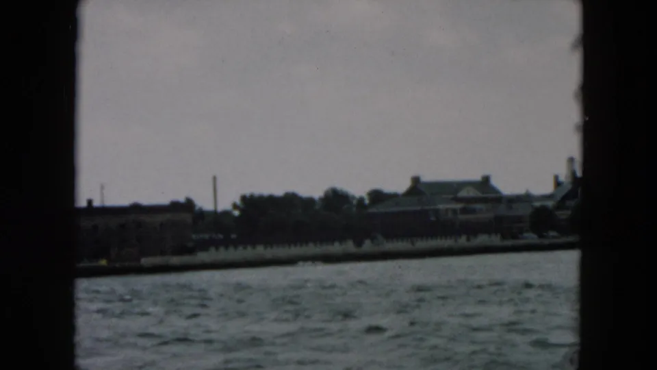 The final frame holds on choppy harbor water, a low shoreline wall, trees, and a waterfront building under a cloudy sky.