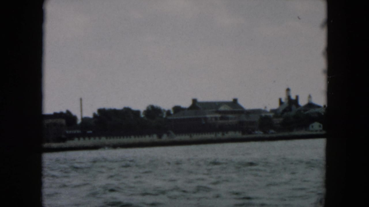Distant shoreline buildings seen across choppy water under an overcast sky.