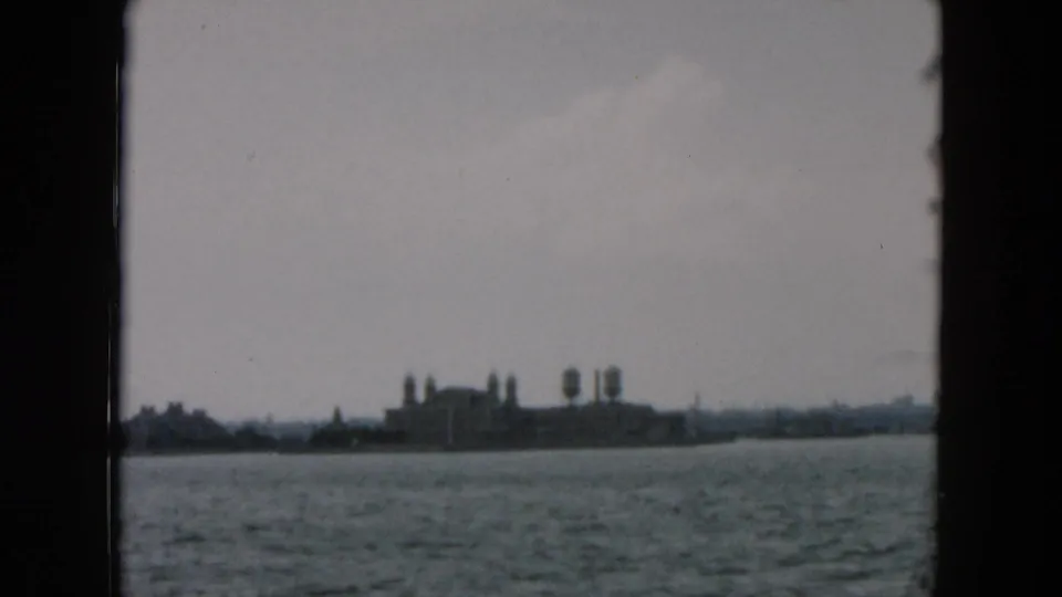 Distant waterfront structures and tower-like forms appear across gray water in this 1957 8mm New York travel shot.