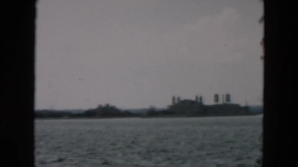 End frame of the 1957 8mm clip showing a hazy shoreline and larger building group across the water from a moving vessel.