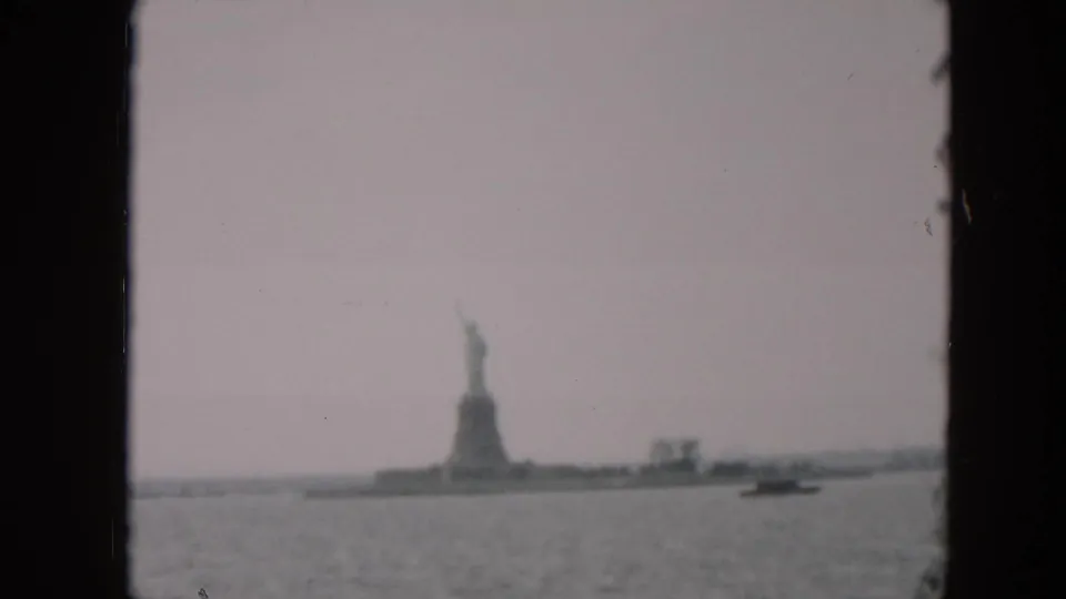 Late frame from a 1957 8mm pan showing the Statue of Liberty across New York Harbor, with a small craft moving in front of Liberty Island.