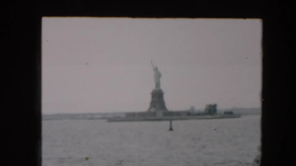 1957 8mm frame showing the Statue of Liberty across New York Harbor, with a channel marker in the foreground water.