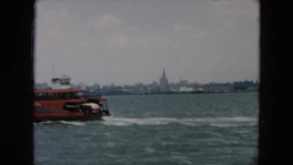 A red ferry exits the frame while the Statue of Liberty appears faintly across the misty harbor.
