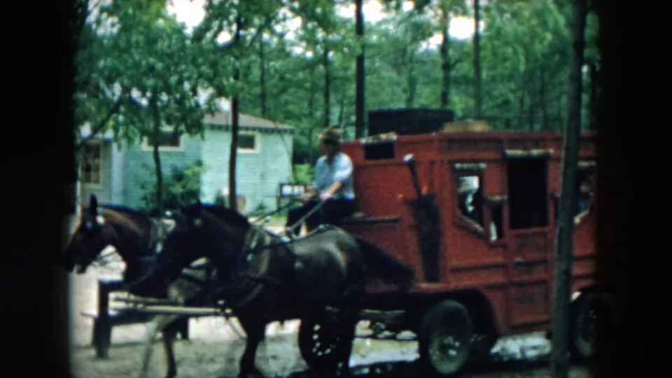 A red stagecoach with visible passengers follows the horse team through the wooded 1957 Hicksville setting.