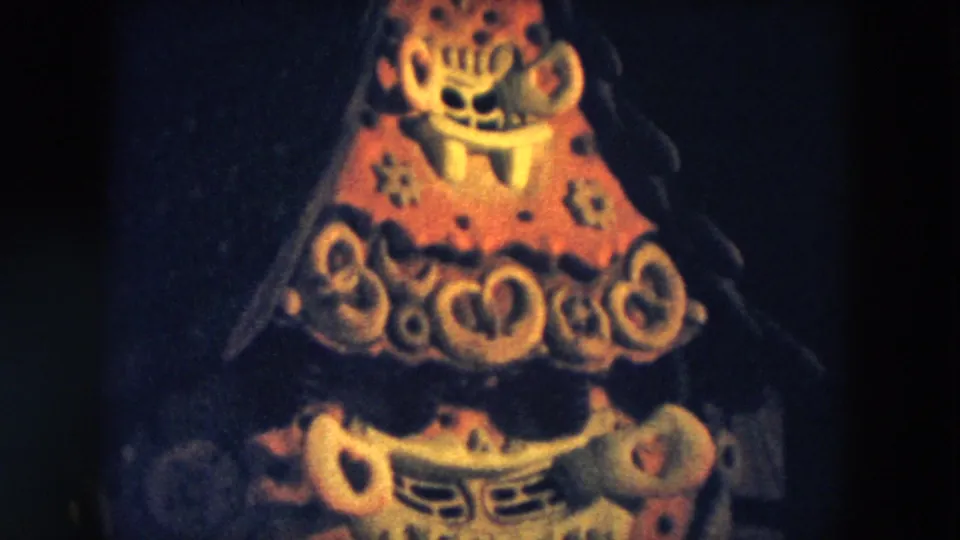 1957 Hicksville 8mm frame showing a red and yellow tiered abstract display with painted mask-like features in low light.