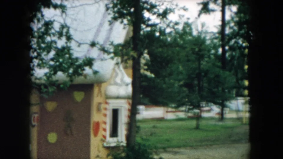 1957 Hicksville home-movie view of the gingerbread-style playhouse, with painted hearts, trim, trees, and an empty park area around it.