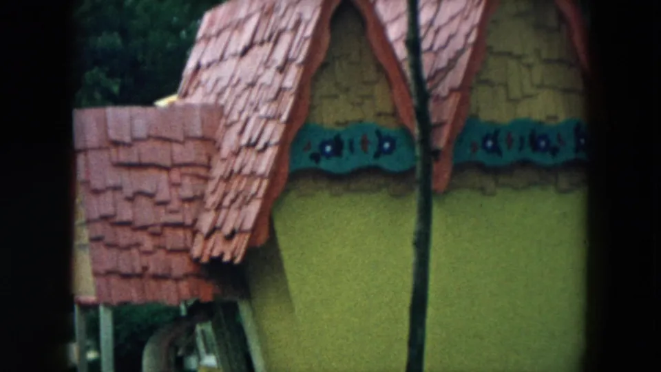 1957 Hicksville frame showing a red shingled roof, yellow wall, curved trim, and tree trunk on a storybook playground structure.