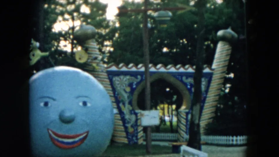 1957 Hicksville frame with the smiling moon sculpture, patterned archway, striped pillars, and a small figure on the roofline.