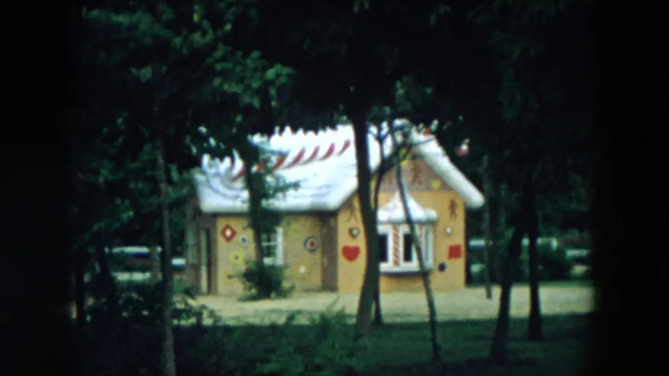 1957 Hicksville frame of the cartoon-style playhouse with painted wall symbols, a white roof, trees, and shaded lawn.