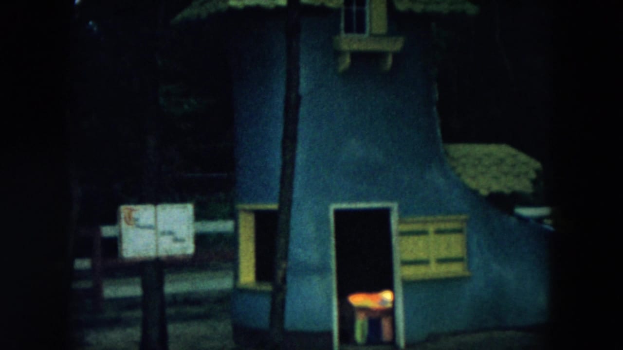 Blue boot-shaped playhouse facade in dark woods with a small glowing opening near the base.