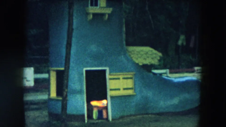 1957 Hicksville frame with the blue boot-shaped playhouse partly blocked by a dark vertical band, with trees and painted trim still visible.