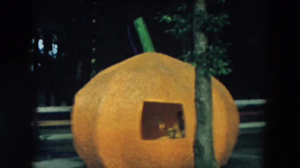 1957 Hicksville home-movie frame showing an orange pumpkin playhouse with a square window partly blocked by a tree.