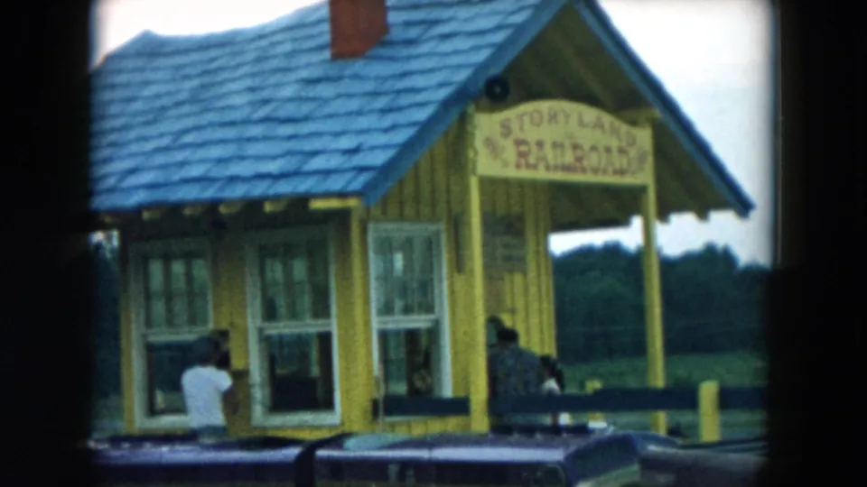 Yellow Storyland Railroad station in Hicksville, New York, with visitors near the ticket windows and a train car in front.