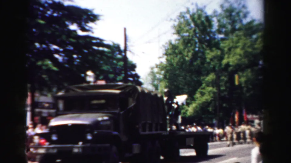 A canvas-covered military truck passes along a tree-lined street during the 1957 Normal, Illinois parade.