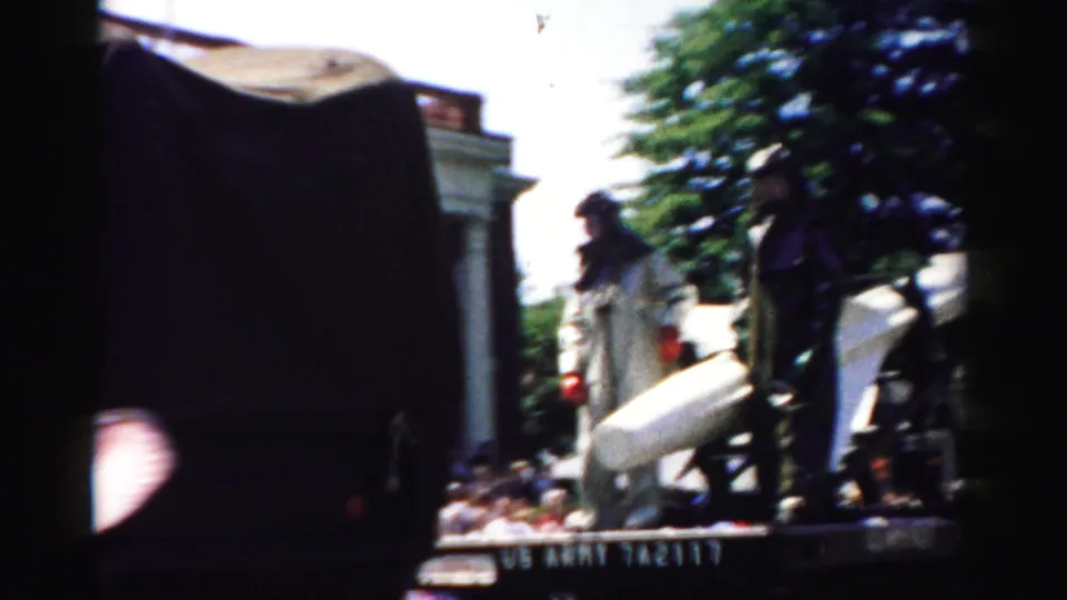 A parade flatbed in Normal, Illinois carries a rocket or missile, with helmeted personnel standing near it.